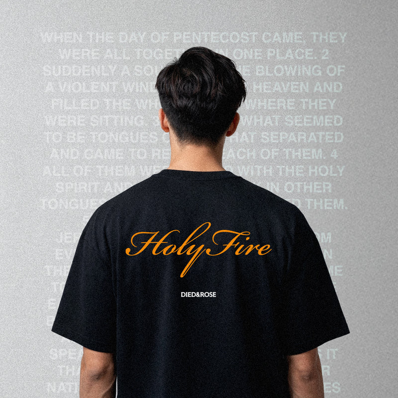 Person wearing a Faith based clothing brand black t-shirt with 'Holy Fire' printed on the back, standing against a gray background with text.