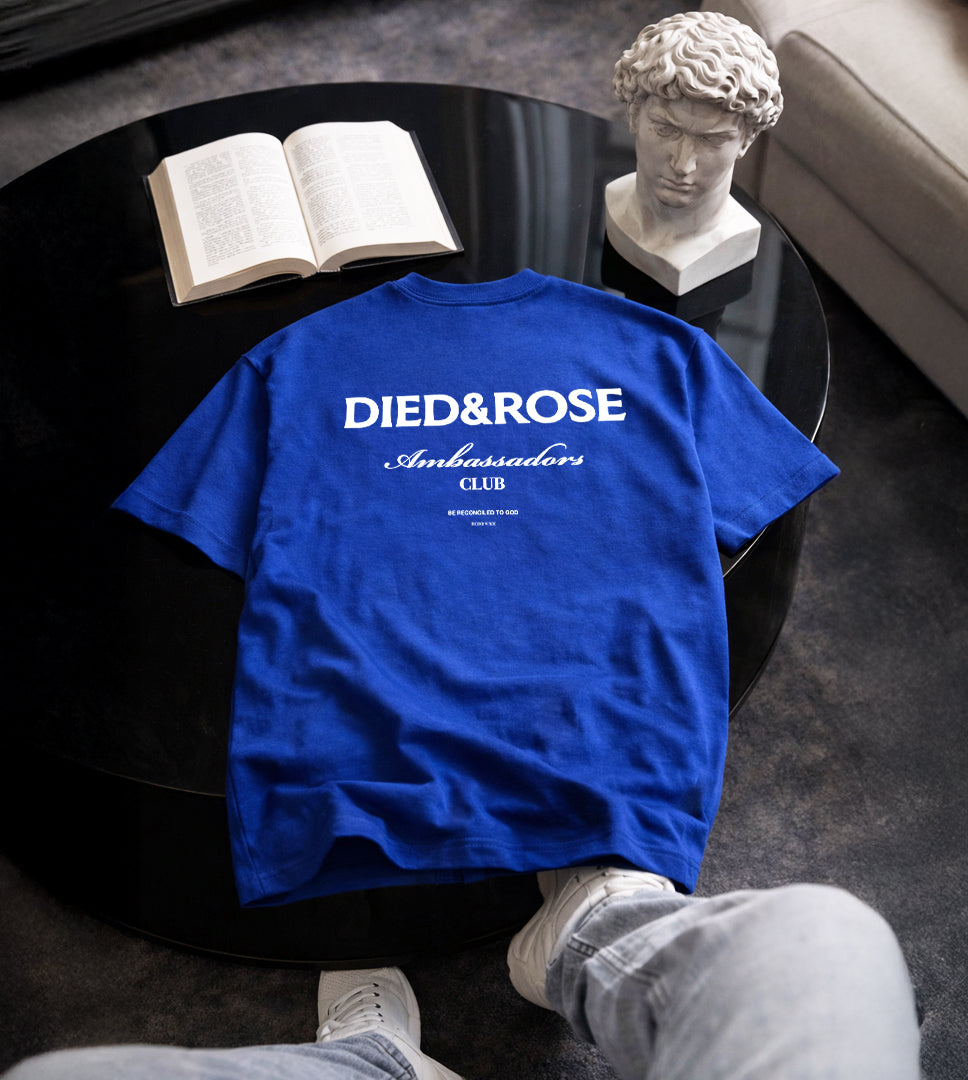 Blue faith based t-shirt with text on a table next to an open book and statue